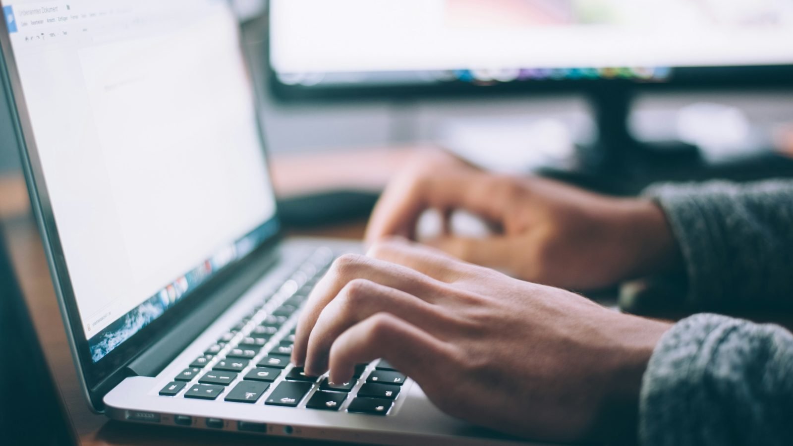 Person using a MacBook Pro on a wooden desk, evoking Coda's clean writing surface